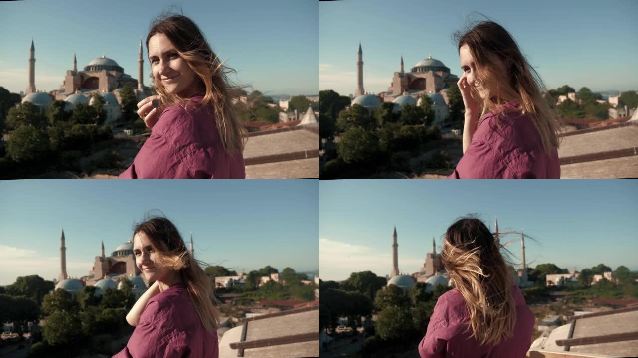 快乐的年轻美丽的旅游女人摆姿势，风吹着头发，在阳光明媚的夏天圣索菲亚大教堂，土耳其。
