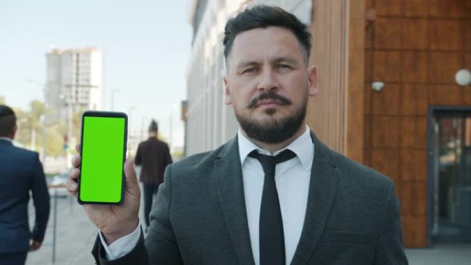 城市街道严肃商人手持色键绿屏智能手机的慢动作肖像