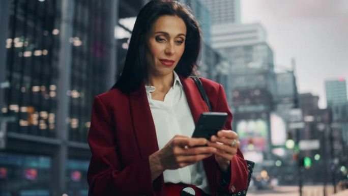 在大城市的街道上使用智能手机的多元化成年女商人的肖像。自信的经理在去办公室的路上与网上的人联系，发信