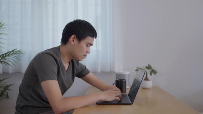 手臂残疾的快乐年轻人在家用笔记本电脑工作。