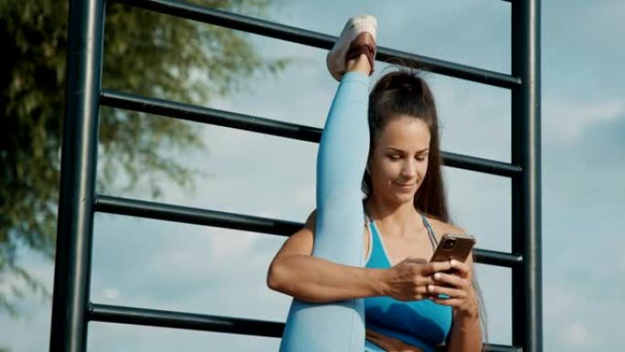 SLO MO运动女子使用智能手机，同时将腿伸向墙壁杆