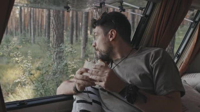 时髦的男人在森林的露营车里享受三明治