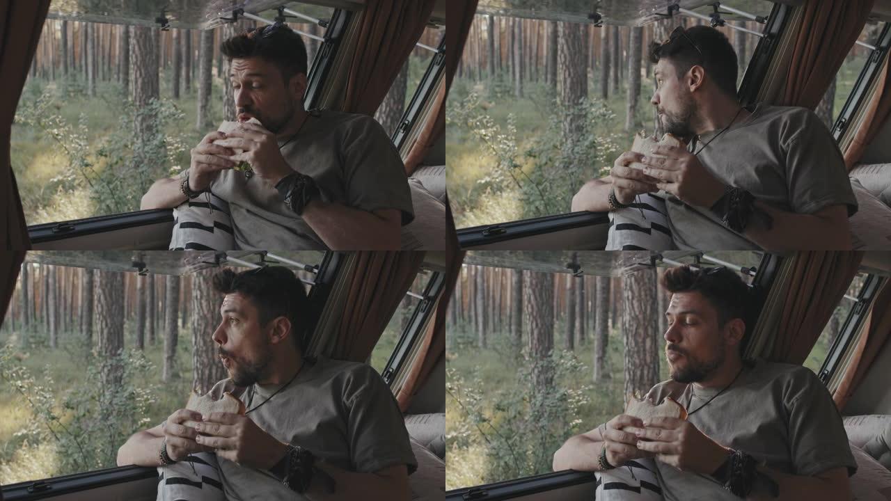 时髦的男人在森林的露营车里享受三明治