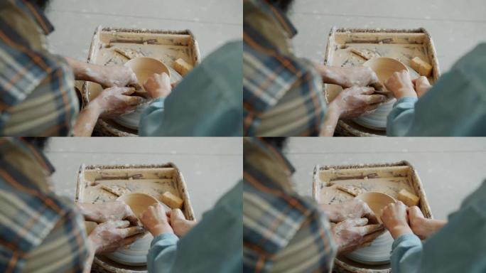 背景图男性和女性双手在投掷轮上的粘土上塑形锅的慢动作