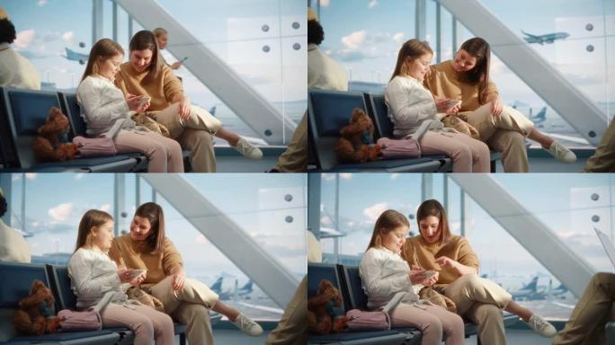 繁忙的机场飞机航站楼: 快乐美丽的母亲和可爱的小女儿等待他们的假期航班，使用移动智能手机进行娱乐和视