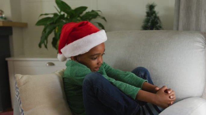 圣诞节时戴圣诞老人帽子的悲伤非洲裔美国男孩坐在沙发上的动画