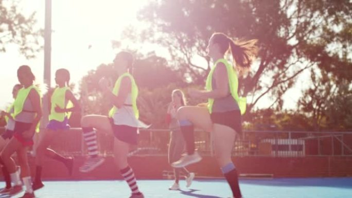 一群女子曲棍球运动员在练习前热身。年轻的曲棍球队在训练比赛前进行热身。曲棍球教练与她的学生一起在球场