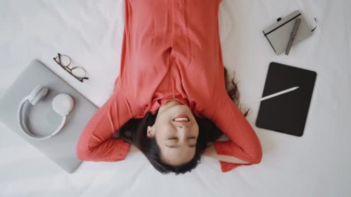 亚洲女人躺在床上仰望白日梦，用笔记本电脑笑得很开心