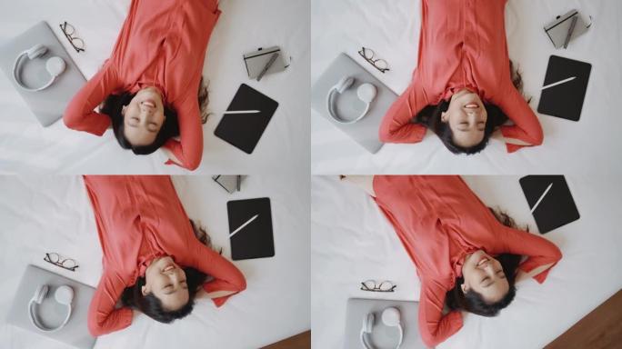 亚洲女人躺在床上仰望白日梦，用笔记本电脑笑得很开心