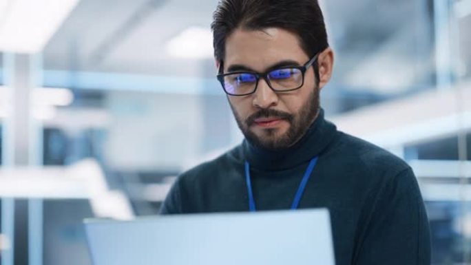一个专业的西班牙裔男子在研发机构工作时使用笔记本电脑的肖像。在开发技术办公室工作的年轻多民族男性工程