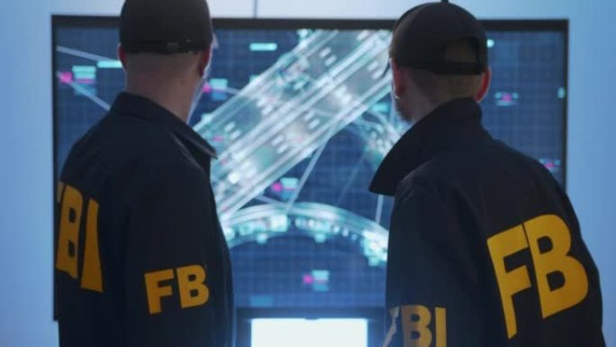 身穿制服的联邦调查局特工在高速公路的安全摄像头记录的HUD屏幕前讨论犯罪分子的路线