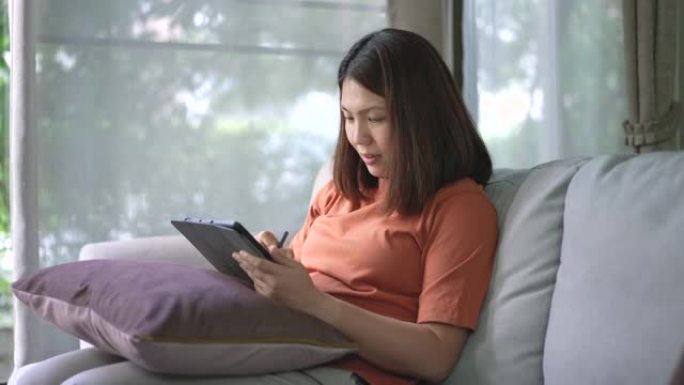 女人在家里的客厅沙发上使用数字平板电脑