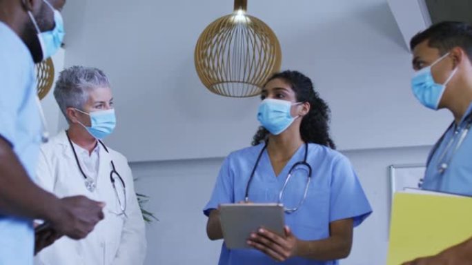 多元化男女医生在口罩上使用平板电脑并在医院进行讨论