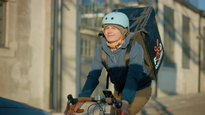穿着保暖背包的食品配送快递员在路上骑自行车为客户和客户交付订单。阳光明媚的日子在现代城市，有时尚的建