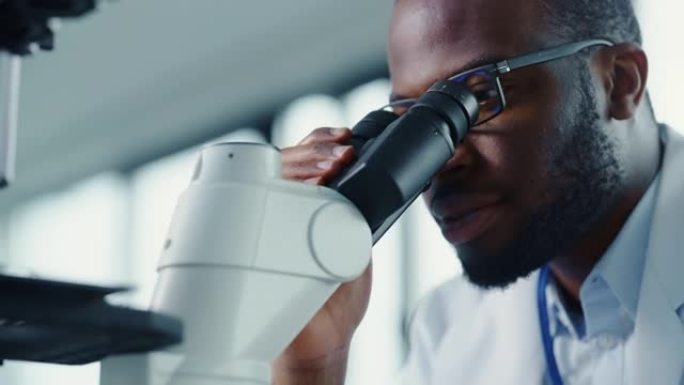 一位黑人男性科学家将带有转基因样品化学物质的培养皿放在显微镜下的特写镜头。用技术设备在现代实验室工作