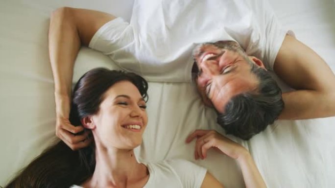 穿着睡衣的年轻新婚夫妇的真实照片是在早上刚醒来的卧室的床上一起休息时，说话和笑很开心。