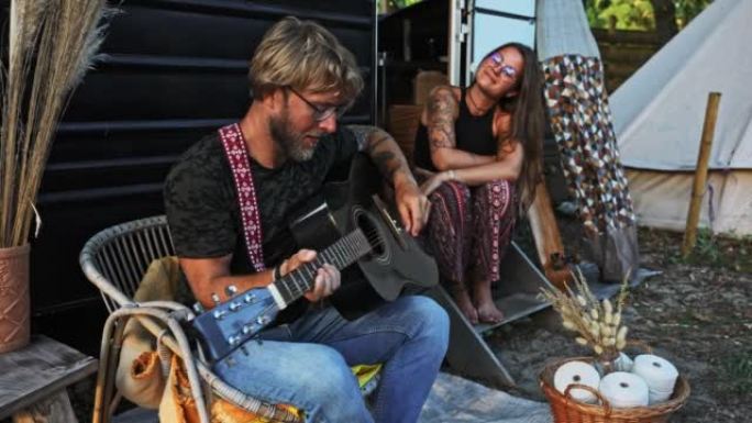 WS年轻的嬉皮士夫妇在老式露营车拖车前弹吉他