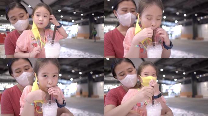 新的正常饮食。亚洲小女孩在餐厅和妈妈喝牛奶前脱下口罩