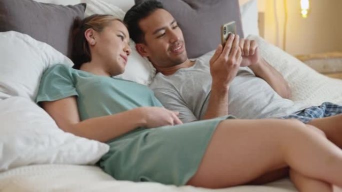 夫妻在床上，社交媒体与智能手机，并在卧室里一起对有趣的在线模因帖子微笑。有电话的快乐男人，有幸福的女