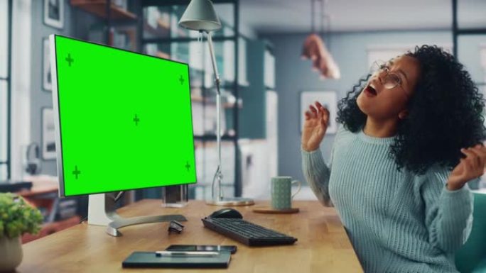 拉丁女性专家坐在家用客厅的台式电脑旁边跳舞，绿屏模拟显示。自由职业者女性在远程工作时玩得很开心。