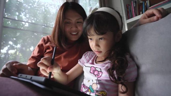 母亲在家在客厅的数字平板电脑上教女儿在线学习