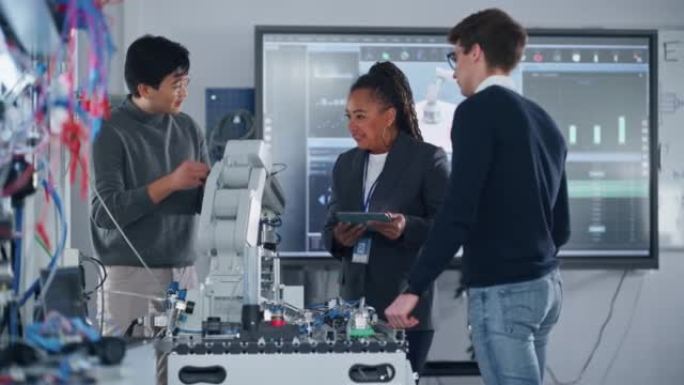 机器人研究实验室的教师和工程师学生会议: 他们聚集在桌子旁，交谈，使用平板电脑并分析工业机器人手臂的