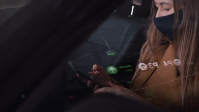 使用智能手机坐在停车场的汽车驾驶员座位上拍摄的年轻快乐美丽的女人戴着口罩的电影照片。