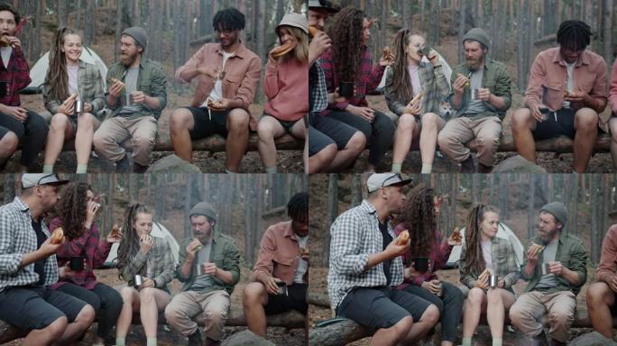多种族的游客在秋天森林的营地里围着火吃饭和喝酒