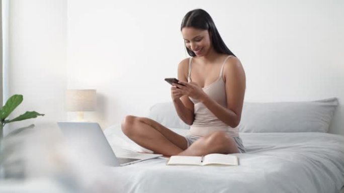 一名年轻女子在家中床上使用智能手机和笔记本电脑的4k视频片段