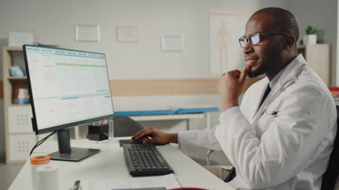 穿着白大褂的富有经验的非裔美国男医生在办公室用个人电脑工作。医疗保健专业人员处理测试结果，病人治疗计