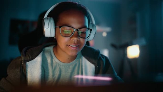 年轻的多种族女孩在家里黑暗舒适的房间里使用笔记本电脑，戴着耳机。她正在网上浏览教育研究。学习科学学校