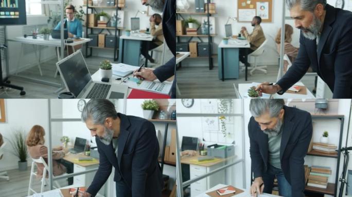 在同事忙于工作的现代办公室中使用笔记本电脑的商人肖像