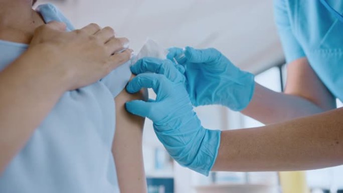 戴着安全手套和防护口罩的医护人员正在健康诊所为女性患者注射疫苗。医生使用皮下注射针和注射器注射药物作