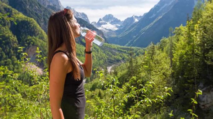 女人俯瞰山谷，背景是山脉，用可重复使用的水瓶补水