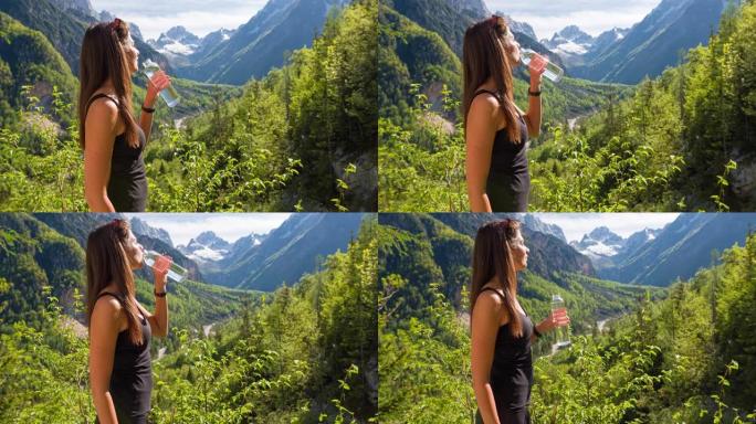 女人俯瞰山谷，背景是山脉，用可重复使用的水瓶补水
