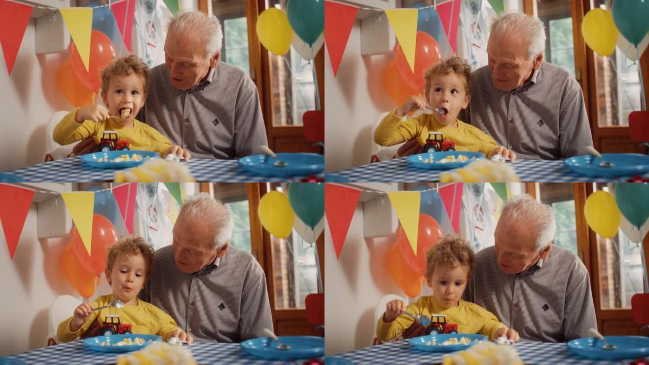 一个可爱的小男孩坐在他爷爷的腿上，吃着美味的生日蛋糕。男孩蹒跚学步，享受着甜蜜的零食和爷爷的温暖和爱