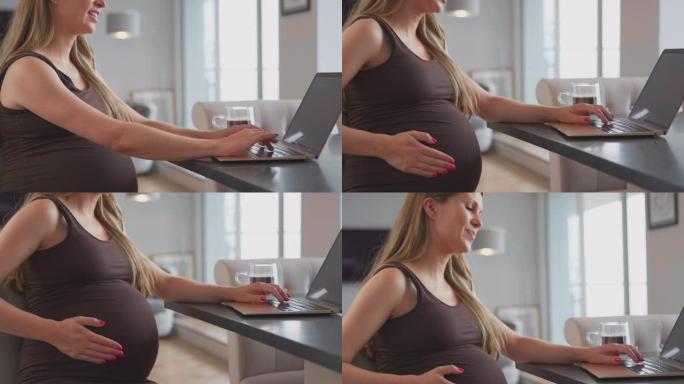 孕妇在家工作，坐在桌子上触摸肚子的笔记本电脑上