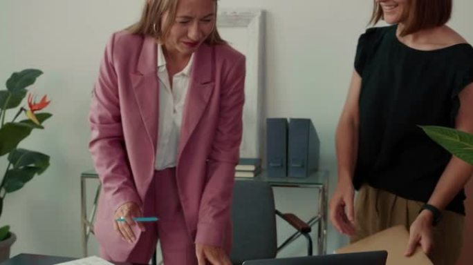 两名漂亮的年轻商务女性进入办公室，与笔记本电脑一起聊天和工作，在现代合作中合作