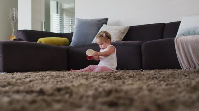 高加索婴儿坐在家里的地板上玩塑料杯