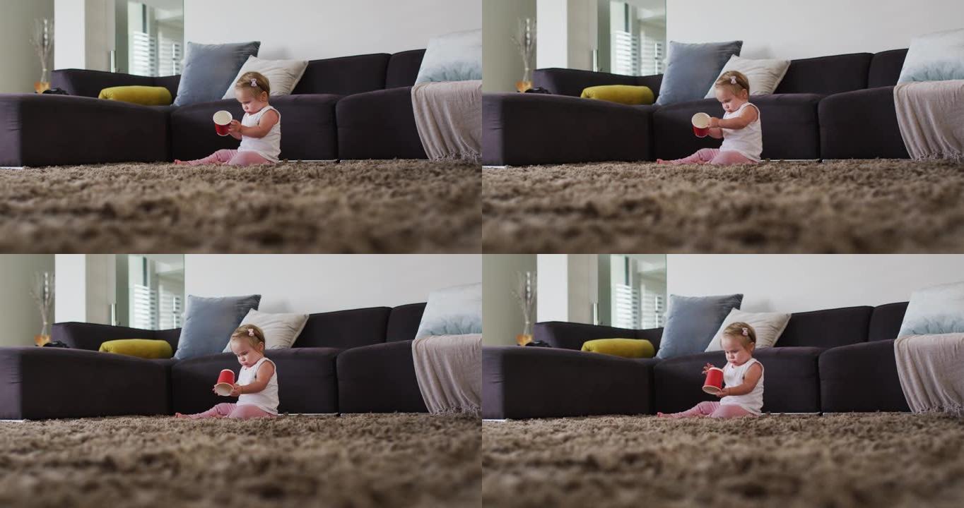 高加索婴儿坐在家里的地板上玩塑料杯