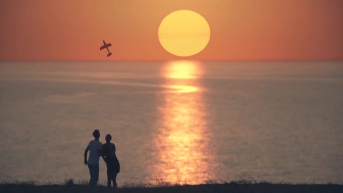 男人和女人把玩具飞机扔在日落背景上。慢动作