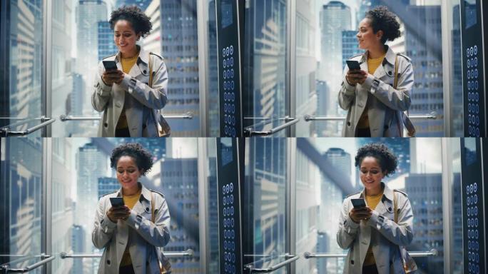 自信的黑人女性乘坐玻璃电梯到现代商务中心的办公室。成功的非洲裔美国经理在使用智能手机时微笑，写短信，