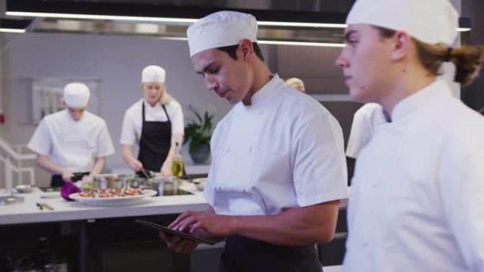 混合种族男厨师在餐厅厨房里穿着白色厨师，用平板电脑看着来