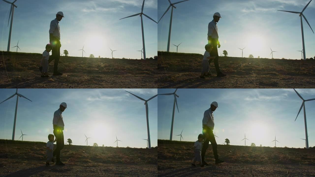 亚洲父亲的剪影日落是工程师，他与15个月大的小男孩牵着手走在风力发电站，一起看着风力涡轮机背景，自由