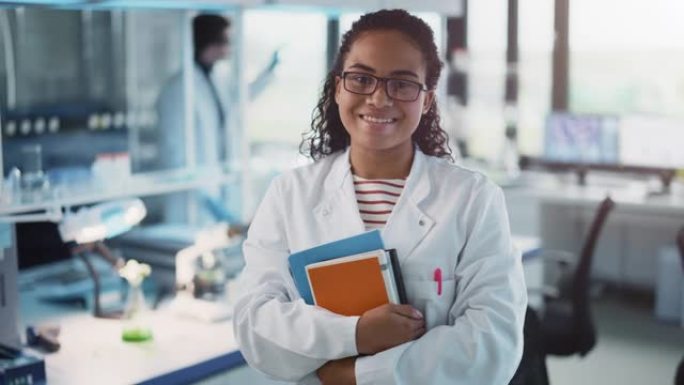 医学科学实验室: 美丽聪明的年轻黑人科学家，穿着白色外套和眼镜，拿着测试书籍，微笑着看着相机。多元化