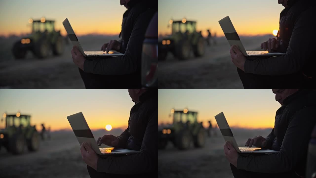 男性农民在日出时在农田的笔记本电脑上工作