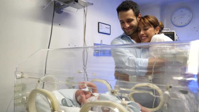 幸福的夫妇在新生儿重症监护病房非常亲切地看着他们的新生儿