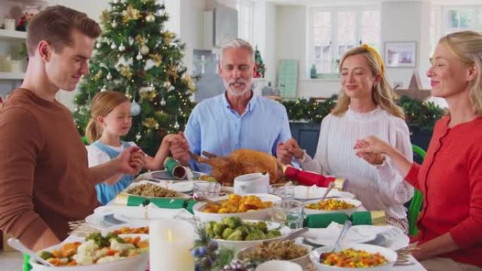 多代家庭在家庆祝圣诞节，一起吃饭前祈祷