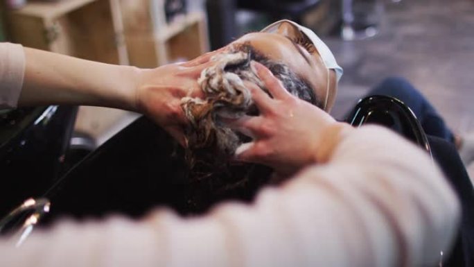 女美发师在美发沙龙洗头的女性顾客戴口罩