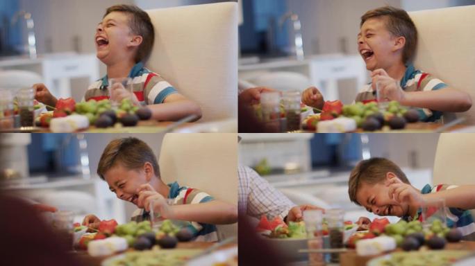快乐的高加索孙子在餐桌旁笑，在家庭用餐时坐在祖父旁边